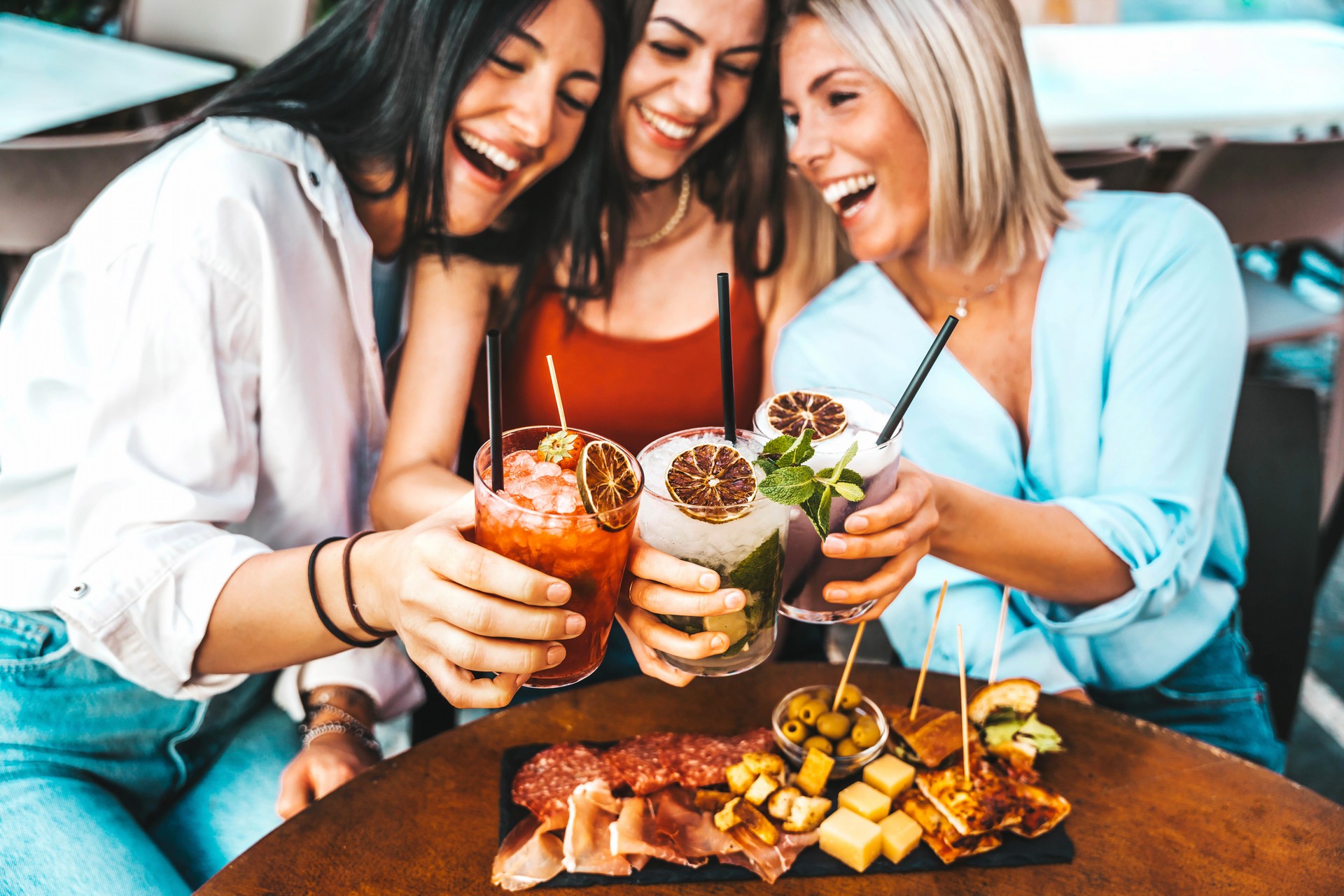 Three beautiful young women drinking cocktails sitting at bar restaurant table - Happy female friends enjoying summertime holidays outdoors - Life style concept with girlfriends hanging out together